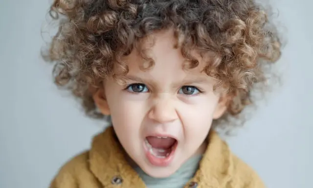 Niño de 1 año con rizos castaños, ojos marrones y expresión de enfado. Las rabietas son parte del desarrollo.