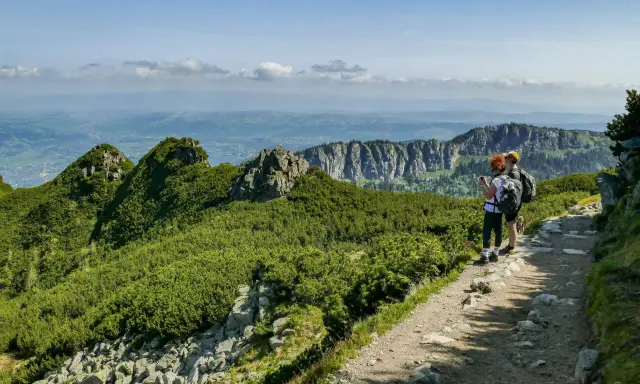 Dwie osoby z plecakami podziwiają widok na Tatry. Szlak jest kamienisty, ale stanowi łatwe zejście z Kasprowego Wierchu.