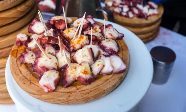 Pulpo a la gallega servido en tabla de madera, con palillos y espolvoreado con pimentón.