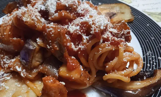 Un piatto invitante di pasta alla norma con melanzane fritte, sugo di pomodoro e ricotta salata grattugiata.