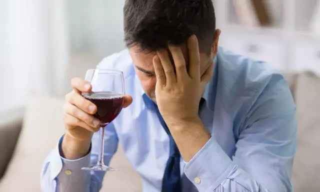 Hombre con copa de vino tinto, con la mano en la frente, buscando alivio en un vino sin histamina.