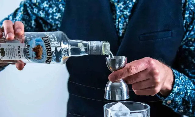 Barman nalewa Żubrówkę do jiggera, przygotowując drinka. W tle szklanka z lodem. Wataha wodka w butelce.