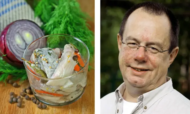En man ler mot kameran bredvid en skål med inlagd sill, en klassisk del av påskbord mat.