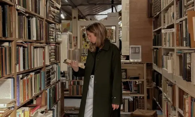 Kobieta w antykwariacie przegląda książki psychologiczne, które zmieniają życie. Wśród regałów pełnych literatury szuka inspiracji.