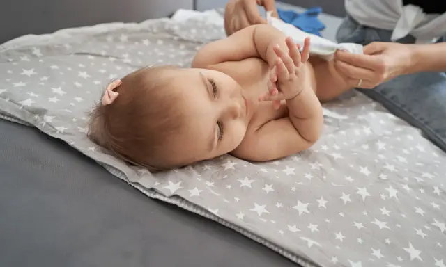 Bebé acostado en una manta con estrellas, mientras le cambian el pañal. Un paso más para dejar el pañal.