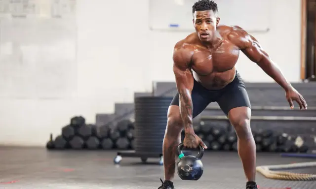 Ein Mann mit starkem Muskelaufbau hebt eine Kettlebell. Seine Anstrengung spiegelt die Ergebnisse von intensiven Trainingseinheiten wider, wie sie in Studien zum Muskelaufbau untersucht werden.