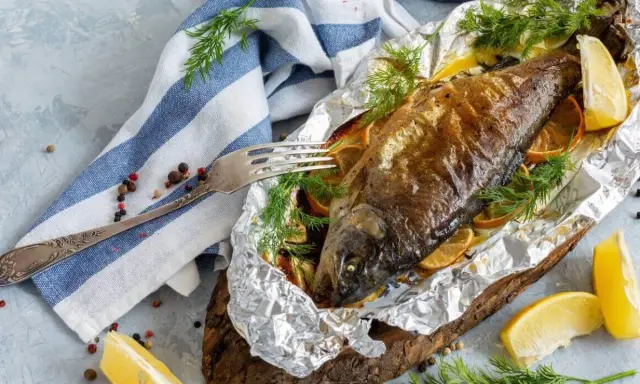 Pieczony pstrąg hodowlany w folii, podany z cytryną i koperkiem. Apetyczny posiłek gotowy do spożycia.