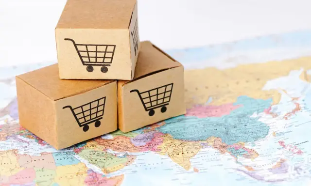 Trzy kartony z ikonami koszyków na zakupy na mapie świata. Symbolizują handel transgraniczny i globalny e-commerce.