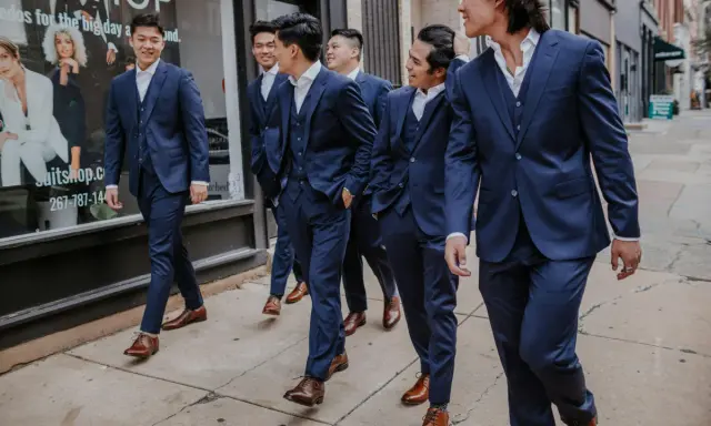 A group of men in navy suits walk down a sidewalk. They are all wearing brown dress shoes, proving you can wear brown shoes with a navy suit.