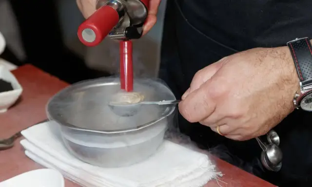 Chef usa sifón para crear texturas aireadas, ideal para recetas de espumas para sifón. Humo frío rodea el bol.
