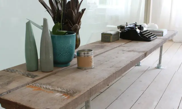 Une table basse rustique, idéale pour savoir que faire avec des vieilles planches de bois. Elle est décorée d'une machine à écrire, de vases et d'une bougie.
