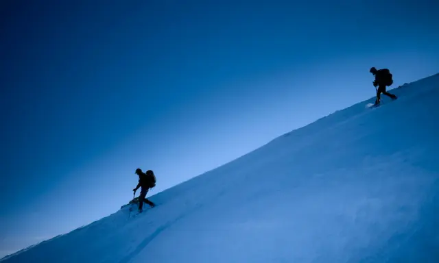 Due escursionisti con ciaspole salgono un pendio innevato sotto un cielo blu intenso. Le ciaspole sono perfette per camminare sulla neve fresca.