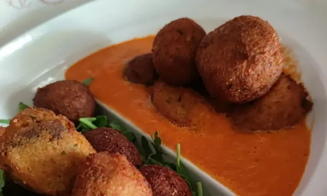 Polpette di pane dorate e croccanti, servite su una salsa rossa cremosa e guarnite con rucola fresca.
