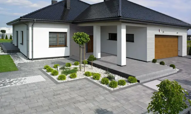 Nowoczesny dom z podjazdem i chodnikiem wykonanymi z różnych rodzajów kostki brukowej, tworzących harmonijną całość.
