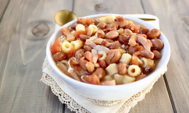 Una ciotola di pasta e fagioli in scatola, con pomodoro e pancetta, servita su un tovagliolo di pizzo.