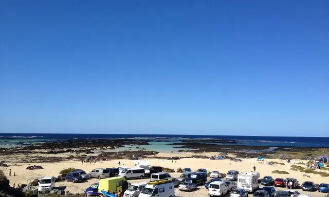 Día soleado en Lanzarote con niños. Coches aparcados en la playa, familias disfrutando del mar y la arena.