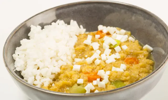Un tazón de arroz blanco junto a un guiso cremoso de lentejas rojas con trozos de queso y verduras.