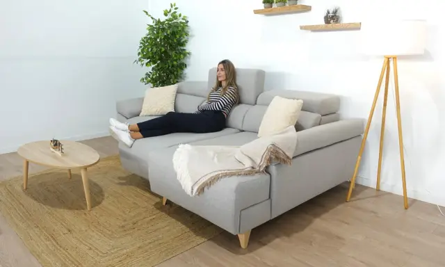 Mujer relajada en un cómodo sofá en medio del salón, con una manta y cojines.