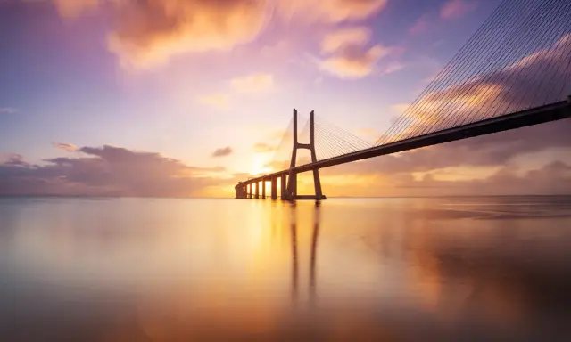 Ponte sospeso sull'acqua calma, con un cielo colorato da un tramonto mozzafiato. Una foto da fare al tramonto, perfetta per catturare la magia del momento.