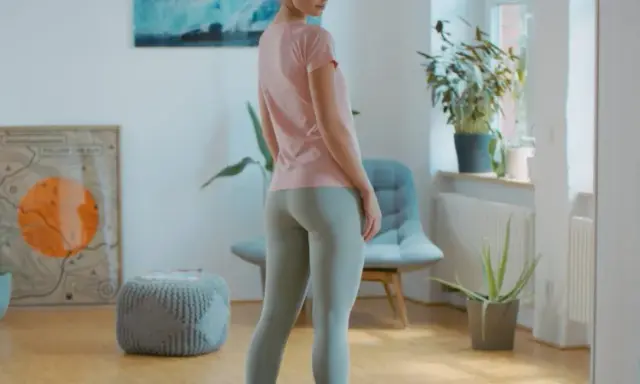 Frau in Sportkleidung, bereit für ein Workout. BWS mobilisieren für mehr Flexibilität. Bücherregal und Pflanzen im Hintergrund.