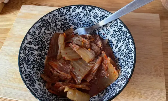 Miseczka z domowym kimchi, widelcem, na drewnianej desce.