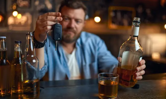 Mężczyzna trzyma kluczyki do samochodu, zastanawiając się, czy jestem pijany. Obok butelki i szklanka alkoholu.