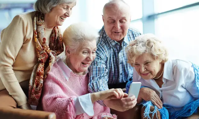 Cztery starsze osoby śmieją się, patrząc na telefon. Może sprawdzają, jak sprawdzić nfz kolejka do sanatorium?