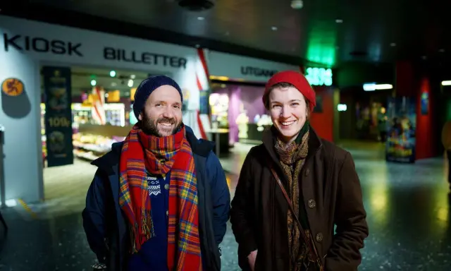 Två glada personer vid en biljettkiosk, redo att se filmer på bio nu.