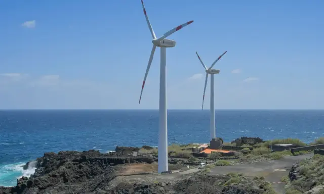Zwei Windräder stehen an einer felsigen Küste Spaniens. Sie sind Teil des Strommixes und erzeugen saubere Energie.