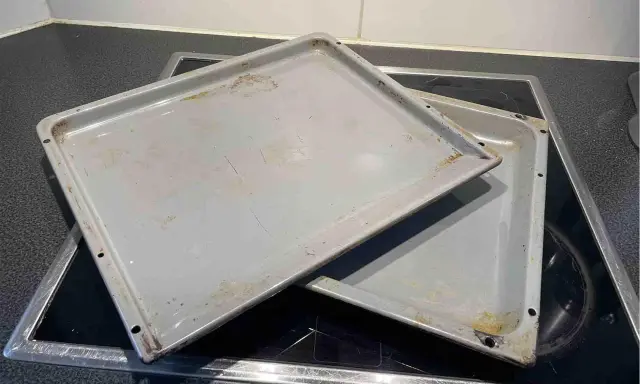 Zwei eingebrannte Backbleche liegen auf einem Cerankochfeld. Zeit, sie zu reinigen und wieder glänzen zu lassen!