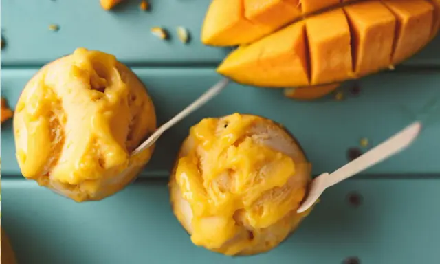 Jak zrobić sorbet? Dwa pucharki z mango sorbetem i kawałki świeżego mango na turkusowym tle.