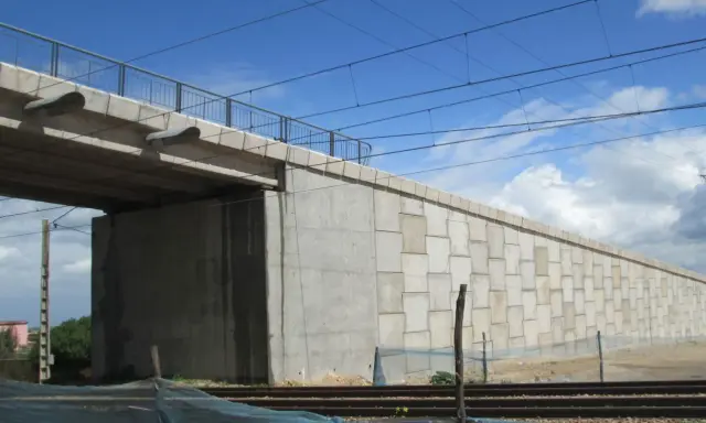 El estribo del puente de hormigón se alza imponente, sosteniendo la estructura sobre las vías del tren.