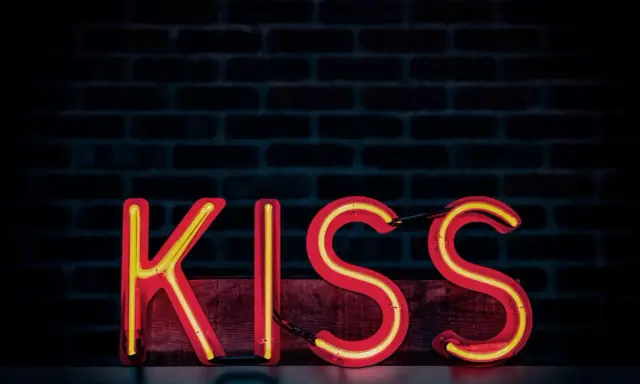 Neonowy napis KISS na tle ceglanej ściany. Zasada KISS: Keep It Simple, Stupid.