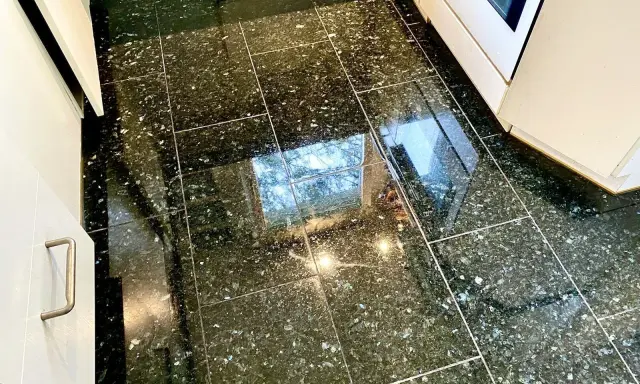 Glänzender Granitboden, der nach dem Granit reinigen strahlt. Spiegelungen von Fenstern und Lichtern auf den dunklen Fliesen.