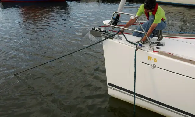 Un homme en gilet de sauvetage ajuste la pendille du bateau, une corde verte s'étendant sur l'eau calme.