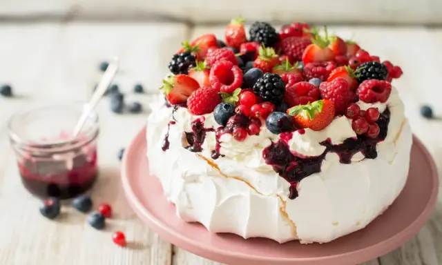 Beza pavlova która zawsze wychodzi, udekorowana bitą śmietaną i mnóstwem świeżych owoców leśnych.