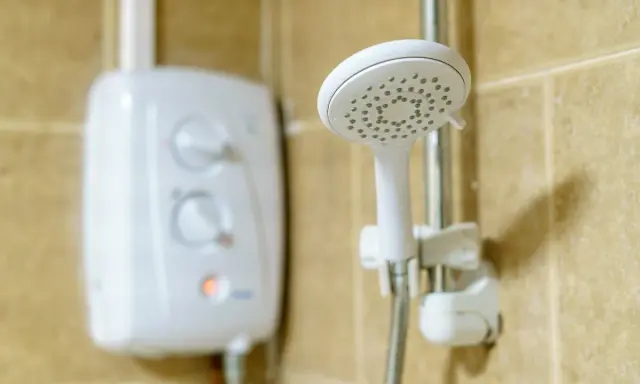 Ein weißer Boiler für die Dusche mit Reglern und eine Duschbrause an der Wand.