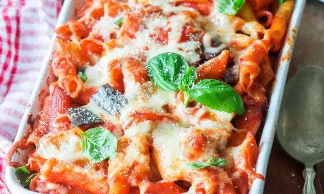 Piatto fumante di pasta al forno con melanzane, ricoperta di formaggio fuso e basilico fresco.