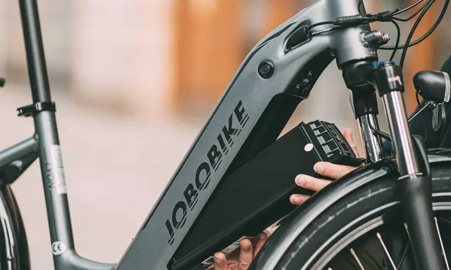Ręce wyjmujące czarną baterię z ramy roweru elektrycznego JOBORBIKE.
