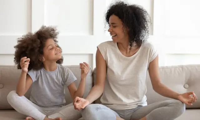 Madre e hija meditando juntas, fomentando sus habilidades de afrontamiento. Ambas sonríen y parecen relajadas.