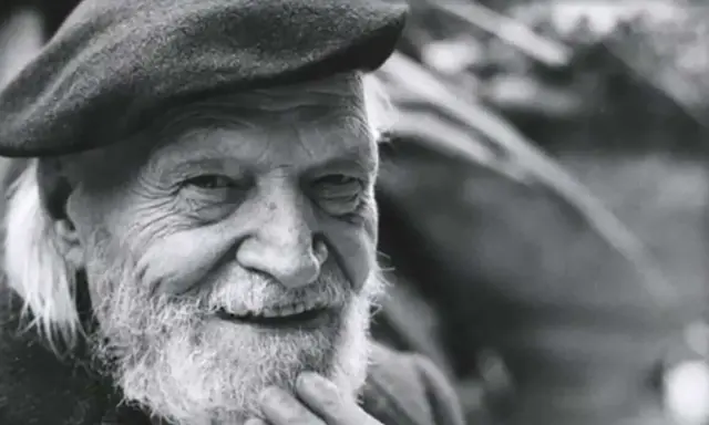 Un anziano con barba e berretto, il suo sorriso saggio evoca il significato che la morte si sconta vivendo appieno ogni istante.