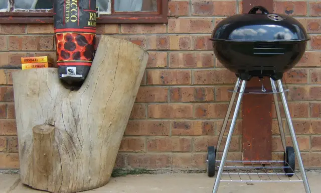 Grill stoi w bezpiecznej odległości od budynku, obok drewnianego pnia z węglem.
