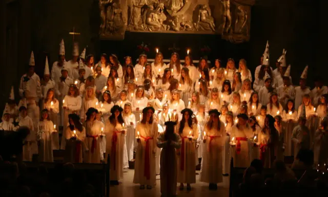 Stor grupp barn och ungdomar i vita kläder och luciakronor, med ljus i händerna, under ett lucia firande i Stockholm.