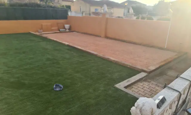 Un terrain de pétanque prêt pour l'entretien, avec une allée en gravier et une pelouse artificielle.