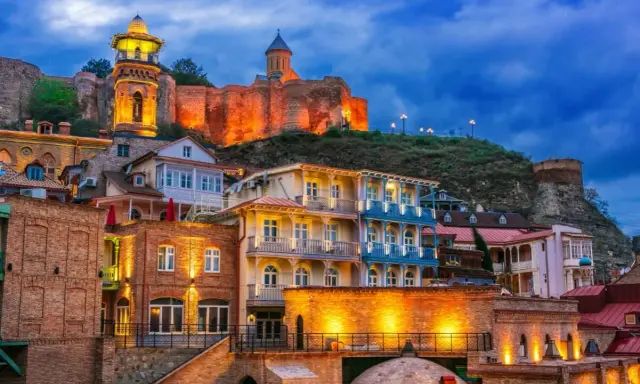 Tbilisi co zobaczyć: malownicze, oświetlone budynki Starego Miasta z widokiem na zabytkową fortecę Narikala i cerkiew na wzgórzu.