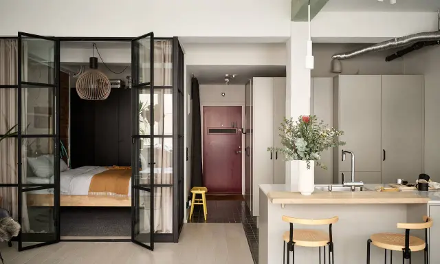 Une chambre en second jour, séparée par des portes vitrées. Une cuisine moderne avec un îlot et des tabourets complète l'espace.