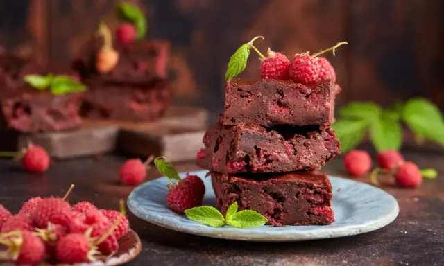 Stos pysznych brownie z malinami, ozdobiony świeżymi malinami i listkami mięty.