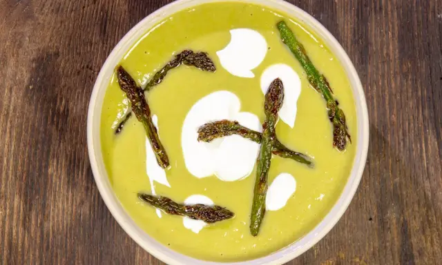 Crema di asparagi vellutata, guarnita con asparagi croccanti e un tocco di panna.