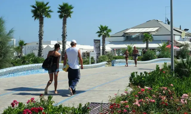 Coppia passeggia sul lungomare del parco mare nord Misano, tra palme e fiori.