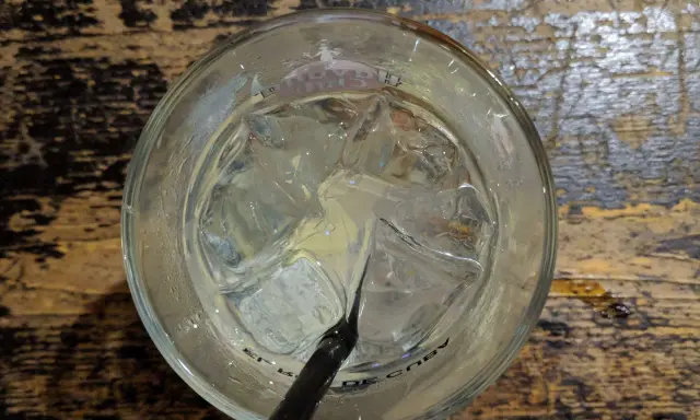 Ein Glas mit Eiswürfeln und einem schwarzen Strohhalm, bereit für einen erfrischenden Gin Tonic auf rustikalem Holztisch.